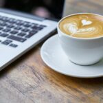 A cup of coffee near a laptop on a desk.
