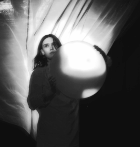PJ Johnson, lead singer of Bug Teeth, photographed in black and white holding a large white ball in front.