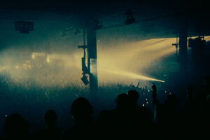 Atmospheric landscape photo taken at the edge of Warehouse Project so that you cansee the crowd, no individual figures, covered in dark club lighting.