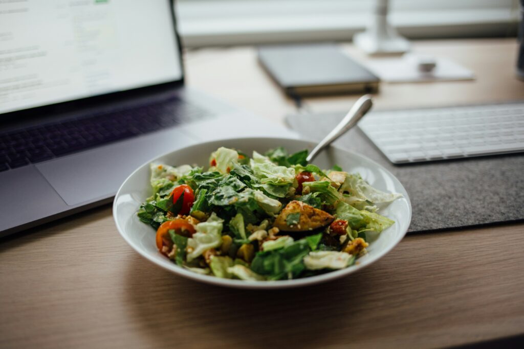 Salad on a desk infront of a laptop screen