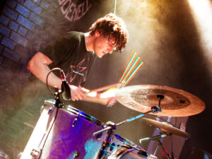 Drummer of Westside Cowboy, Paddy Murphy, mid-hit of the drum. The shutter speed of the camera has made the drumstick look like it's split into four - a cool effect. The angle is from lower down so one of the drums appears larger.