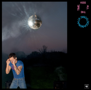 The album cover for Harry Styles' upcoming 2026 album 'Kiss All The Time. Disco, Occasionally'. It features a dark image shot outside with harry brightly lit in the corner wearing goggles, a blue t-shirt and jeans. In the night sky, there is, moon-like, a large glittering disco ball.