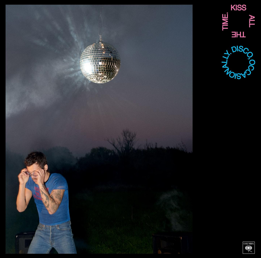 The album cover for Harry Styles' upcoming 2026 album 'Kiss All The Time. Disco, Occasionally'. It features a dark image shot outside with harry brightly lit in the corner wearing goggles, a blue t-shirt and jeans. In the night sky, there is, moon-like, a large glittering disco ball.