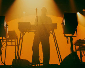Picture taken from a low angle of Barry Can't Swim at the DJ decks. Any distinguishable features are obscured by the high levels of contrast in the photo and the hazy orange nightclub lighting.