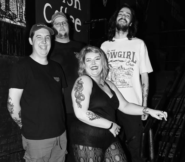 Box Wine band members standing, smiling at what looks like outside a venue. The photo is in B+W.