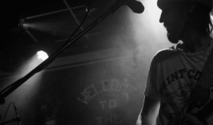 Dark and shadowy black and white picture of the gig. You can make out the mic, one of the bandmembers and the iconic 'Welcome To The Brudenell' text which is on the back of the stage.