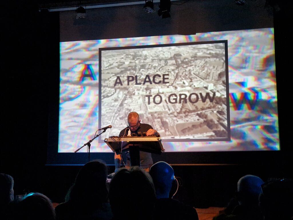 photo of Warrington-Runcorn New Town Development Plan performing onstage in front of a screen that reads 'A PLACE TO GROW'.