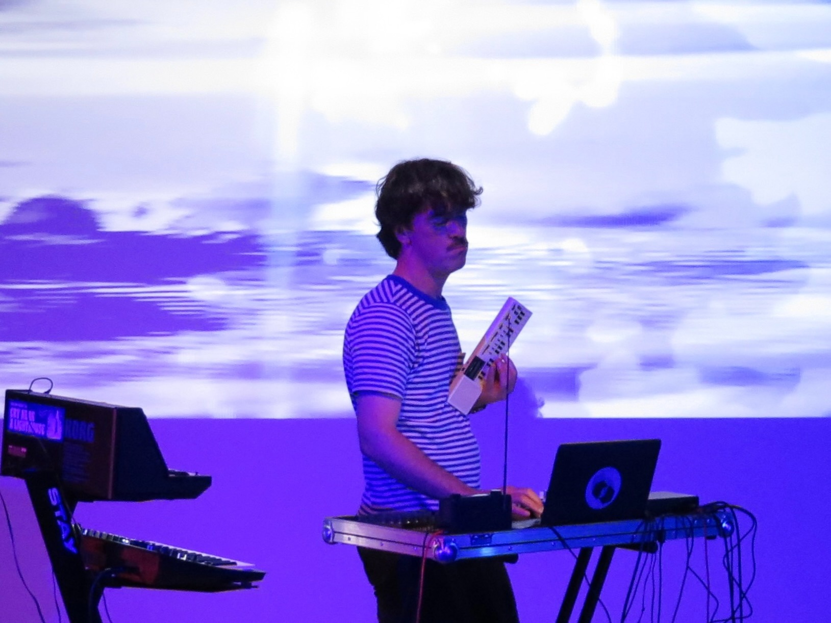 Picture of James Adrian Brown playing the synth deck gently holding his Casio toy synthesiser, his eyes closed.